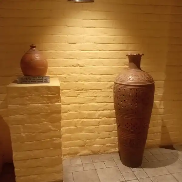 Two clay vases displayed on a plinth and the floor against a lit yellow brick wall