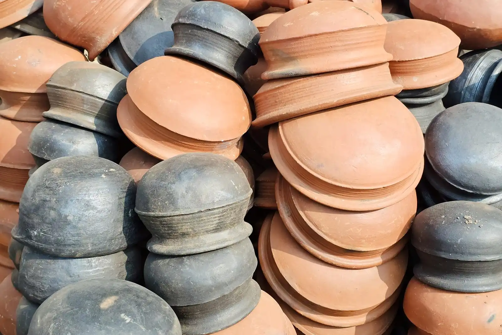 A heap of terracotta and grey clay pots with lids