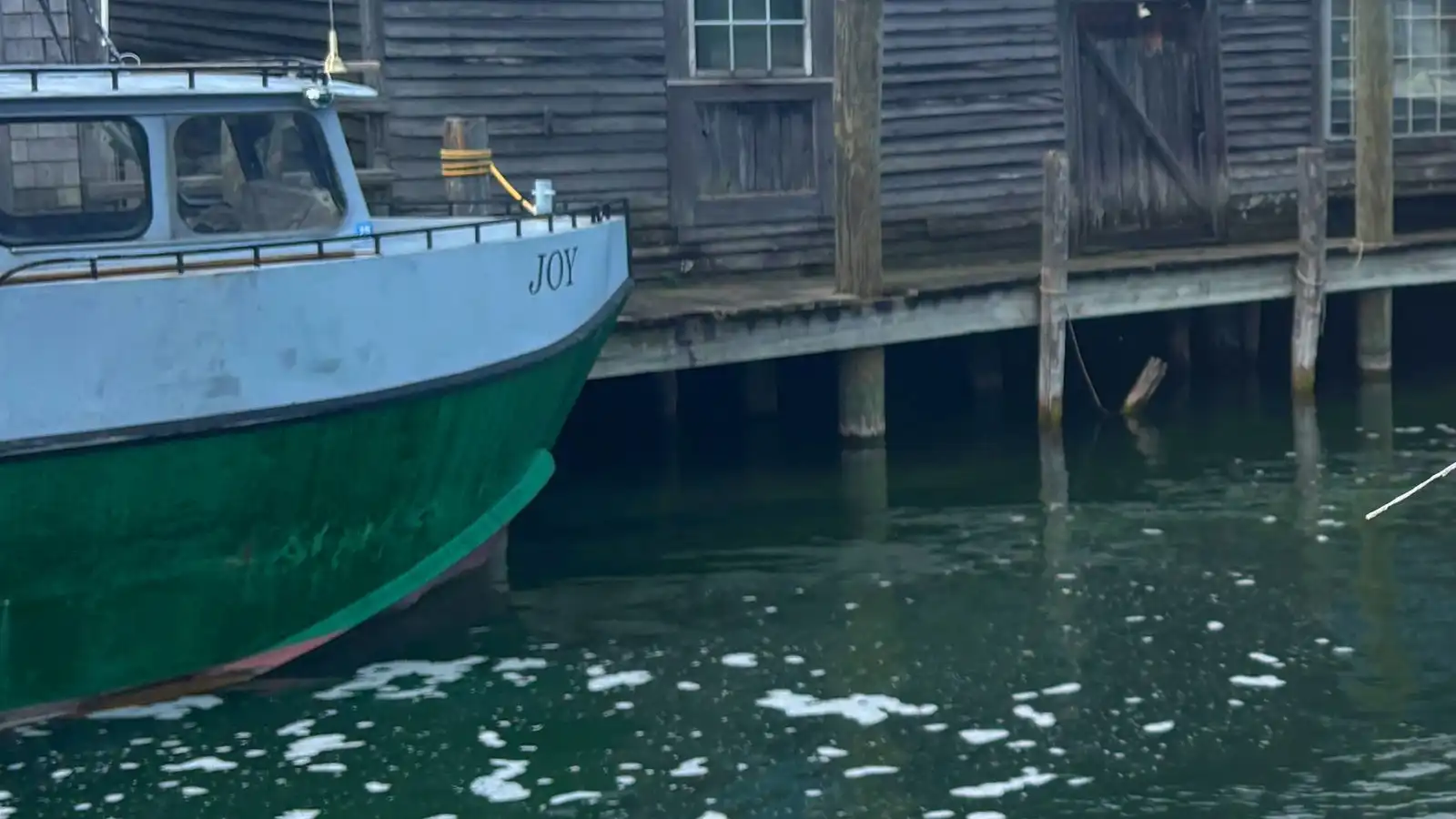A small green and white boat moored beside weathered wooden boathouses with green roofs