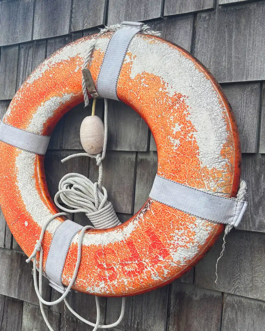 A faded orange life ring hanging on a shingled wall beside a harbour