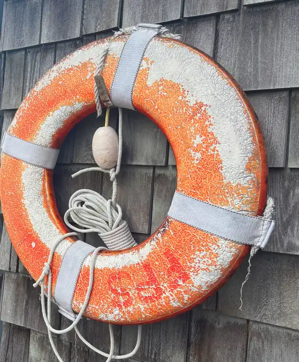 A faded orange life ring hanging on a shingled wall beside a harbour