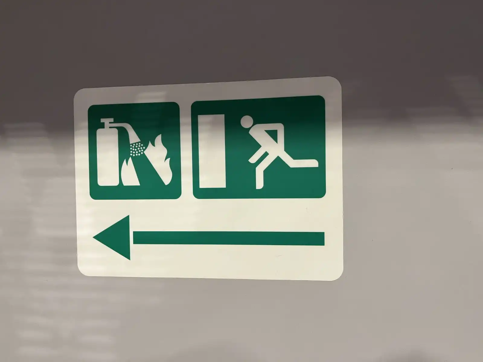 A green safety sign with pictograms and a white arrow pointing left