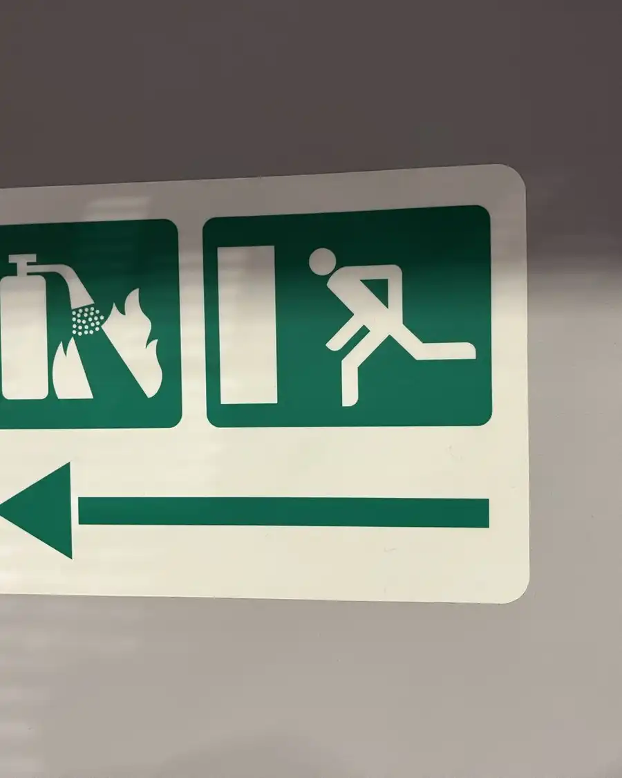 A green safety sign with pictograms and a white arrow pointing left