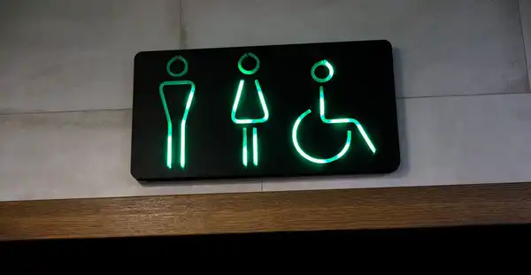 A black sign with glowing green restroom and wheelchair pictograms