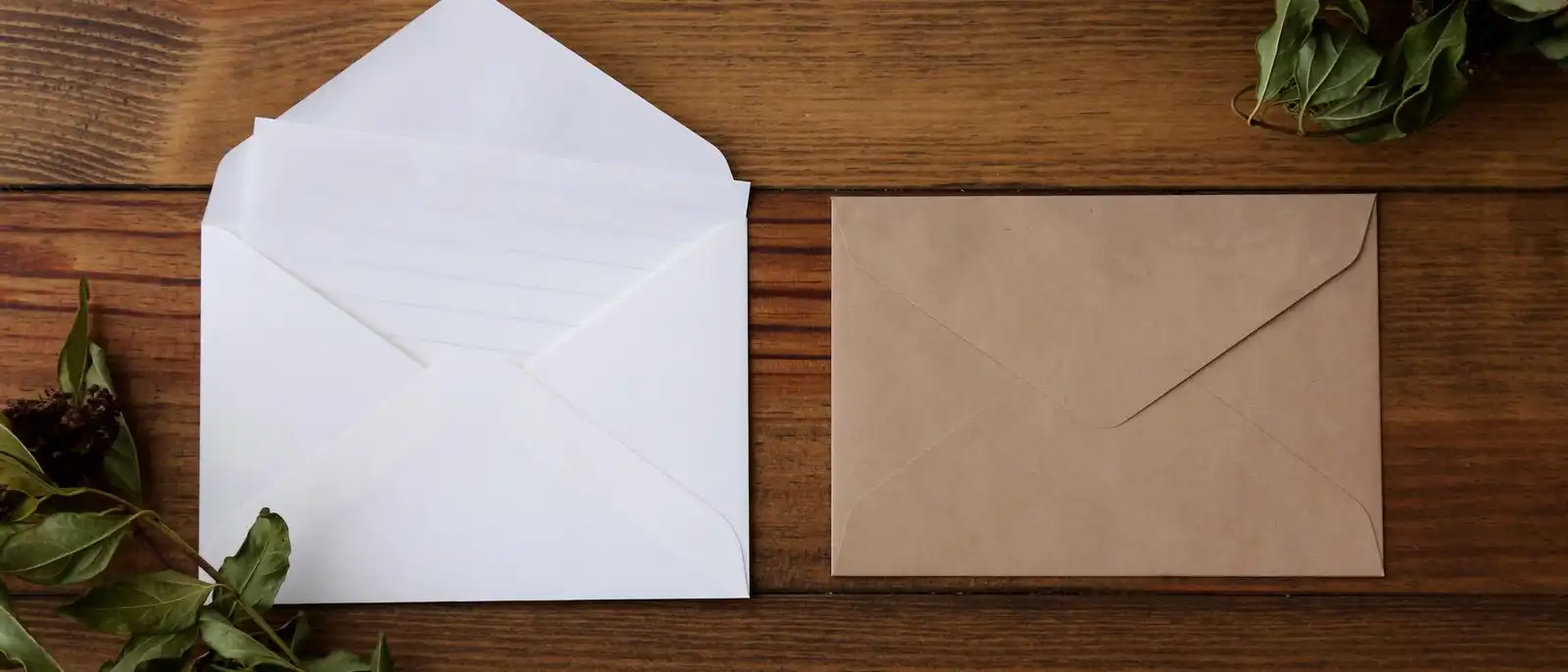 An open white envelope and a brown kraft envelope on a dark wooden table