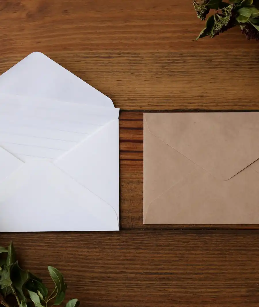 An open white envelope and a brown kraft envelope on a dark wooden table