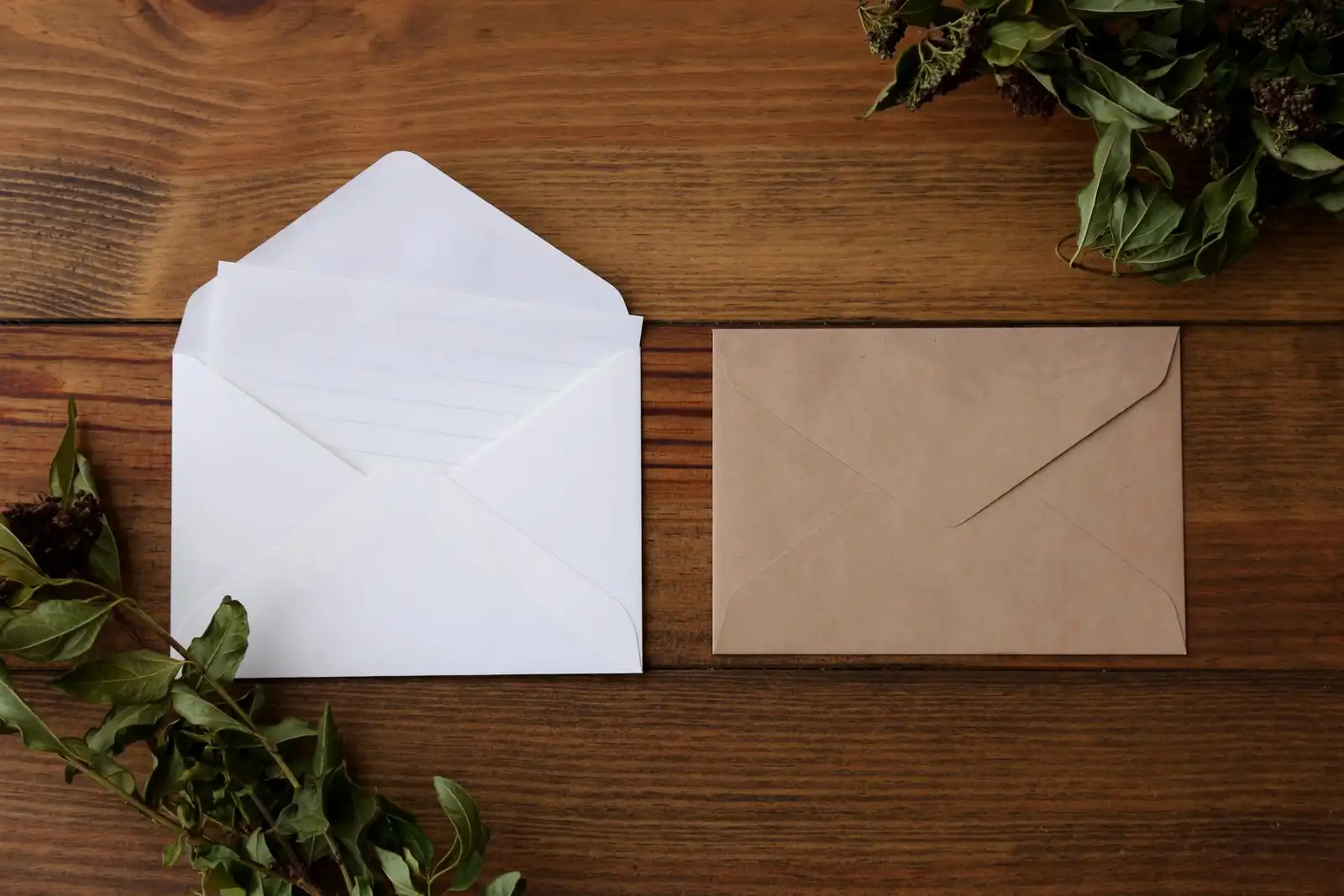 An open white envelope and a brown kraft envelope on a dark wooden table
